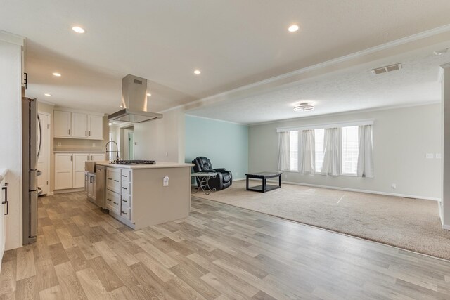 kitchen with a kitchen island with sink, white cabinets, island range hood, light carpet, and appliances with stainless steel finishes