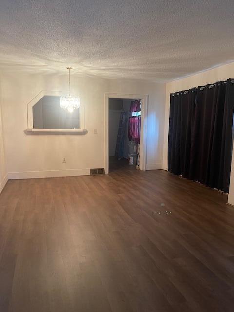 empty room featuring a textured ceiling, dark hardwood / wood-style floors, and a notable chandelier