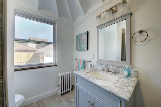 bathroom with vanity, toilet, hardwood / wood-style floors, radiator heating unit, and vaulted ceiling