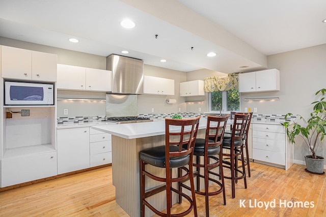 kitchen featuring white cabinets, wall chimney exhaust hood, and light hardwood / wood-style floors