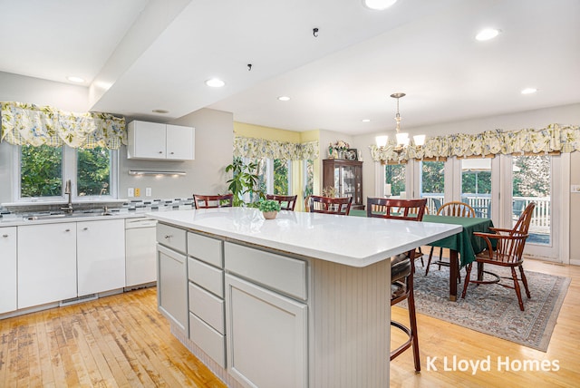 kitchen featuring a breakfast bar area, white dishwasher, light wood-type flooring, a center island, and sink