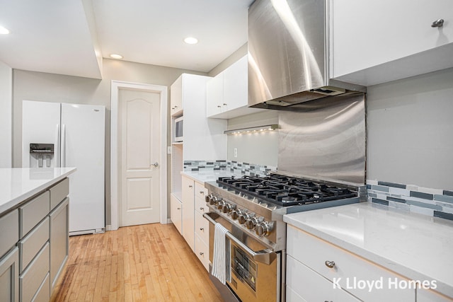 kitchen featuring light hardwood / wood-style floors, white cabinetry, white refrigerator with ice dispenser, high end range, and wall chimney range hood