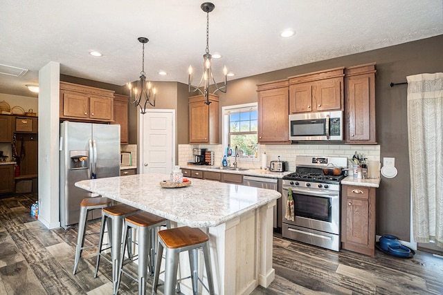 kitchen with appliances with stainless steel finishes, a breakfast bar, a kitchen island, dark hardwood / wood-style flooring, and an inviting chandelier