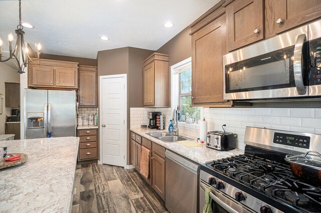 kitchen featuring dark wood-type flooring, sink, an inviting chandelier, stainless steel appliances, and decorative light fixtures