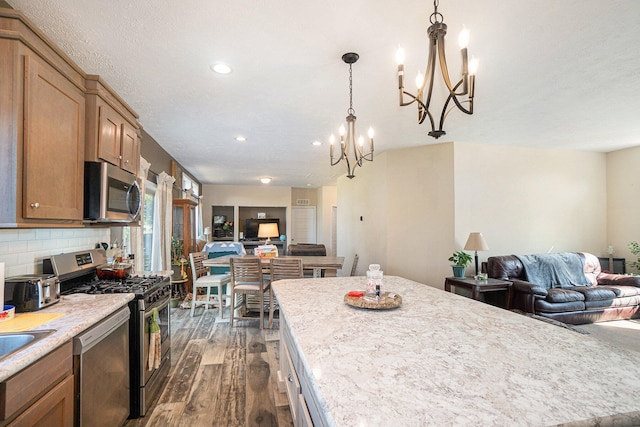 kitchen with dark hardwood / wood-style floors, hanging light fixtures, an inviting chandelier, stainless steel appliances, and backsplash