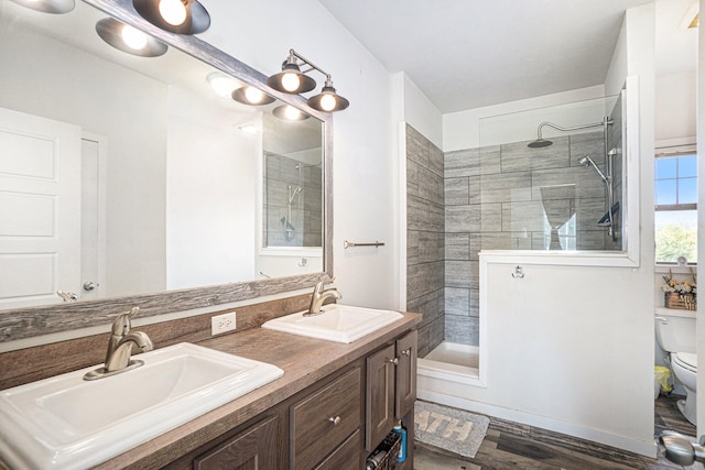 bathroom with a tile shower, hardwood / wood-style flooring, vanity, and toilet