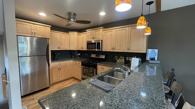 kitchen featuring pendant lighting, stainless steel appliances, dark stone countertops, light brown cabinetry, and backsplash