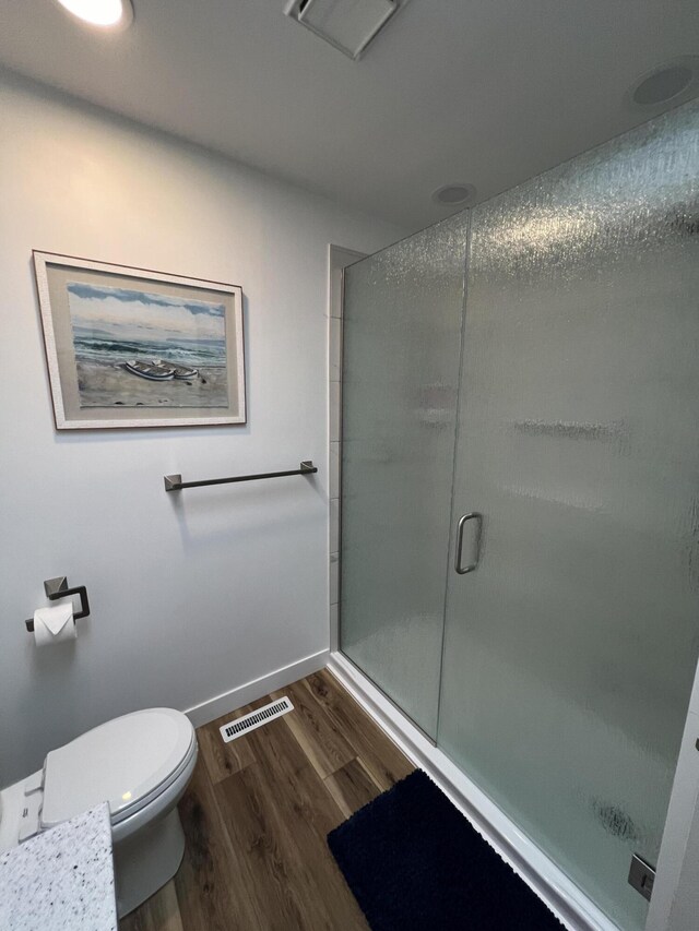 bathroom with hardwood / wood-style floors, toilet, and a shower with door