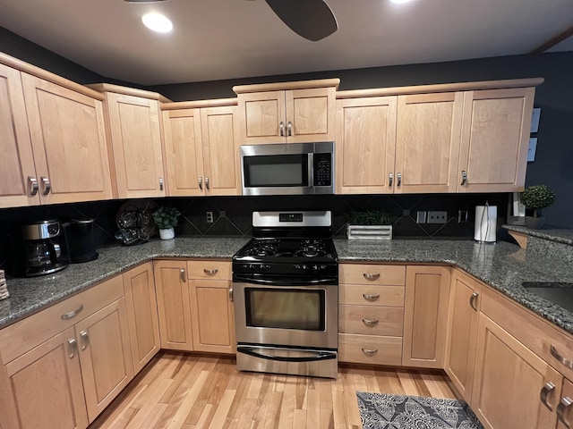 kitchen with light wood-type flooring, stainless steel appliances, dark stone countertops, and backsplash