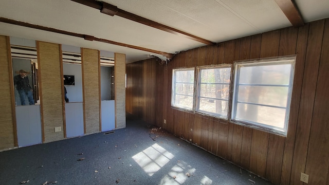 spare room featuring beamed ceiling, a textured ceiling, and wood walls