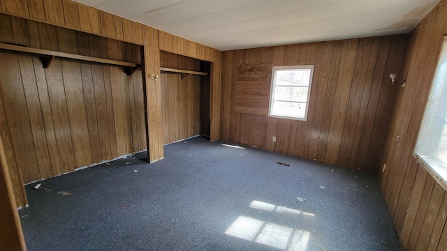 unfurnished bedroom featuring dark colored carpet, wooden walls, and two closets