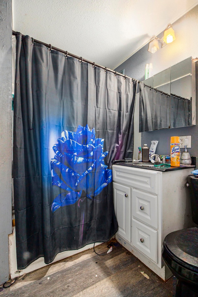 bathroom featuring vanity, wood-type flooring, a textured ceiling, walk in shower, and toilet