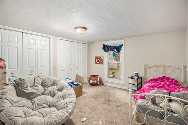 bedroom with a textured ceiling, multiple closets, and carpet floors