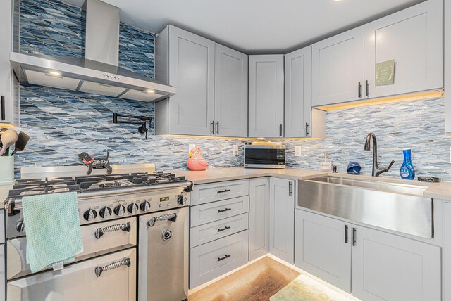 kitchen featuring decorative backsplash, light hardwood / wood-style flooring, wall chimney range hood, and sink