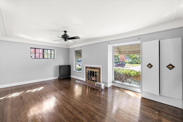 unfurnished living room with radiator heating unit, dark hardwood / wood-style flooring, ceiling fan, and a brick fireplace