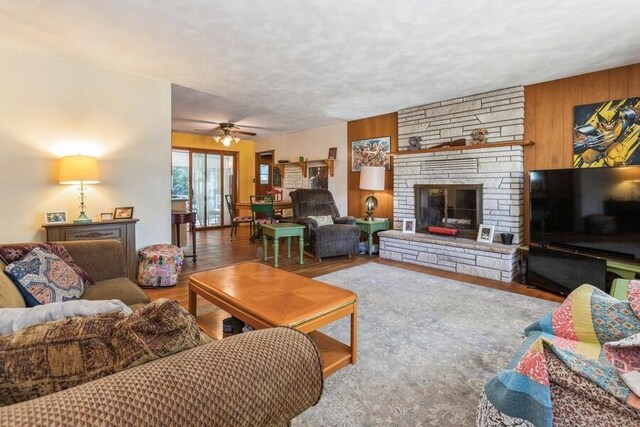 living room with ceiling fan, a stone fireplace, wood walls, and hardwood / wood-style floors