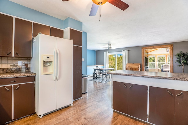 kitchen featuring dark brown cabinets, light wood-type flooring, white refrigerator with ice dispenser, backsplash, and ceiling fan