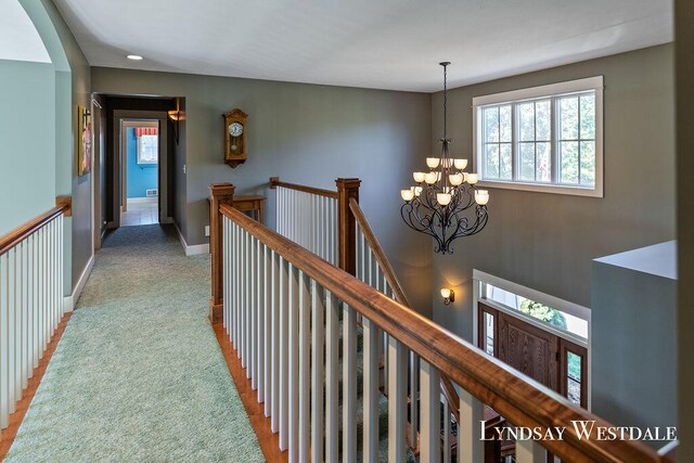 corridor featuring an inviting chandelier and light colored carpet