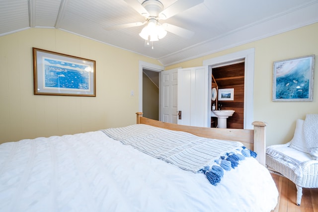 bedroom featuring ceiling fan, lofted ceiling, wooden walls, hardwood / wood-style flooring, and ensuite bathroom