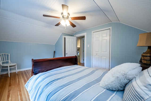 bedroom featuring a closet, vaulted ceiling, wood walls, hardwood / wood-style floors, and ceiling fan