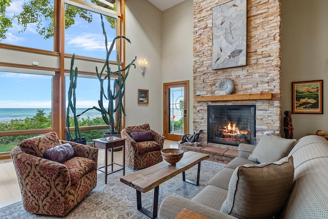 living room with a high ceiling, a fireplace, a water view, and light hardwood / wood-style flooring