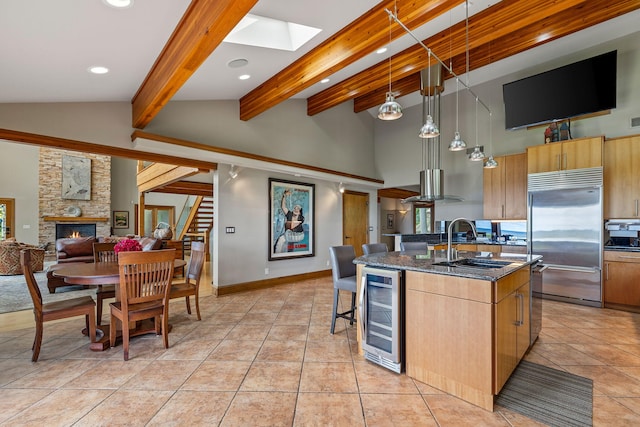 kitchen with stainless steel built in refrigerator, wine cooler, beam ceiling, a kitchen island with sink, and decorative light fixtures