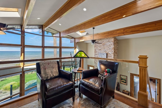 living area with a water view, a stone fireplace, vaulted ceiling with skylight, ceiling fan, and hardwood / wood-style floors