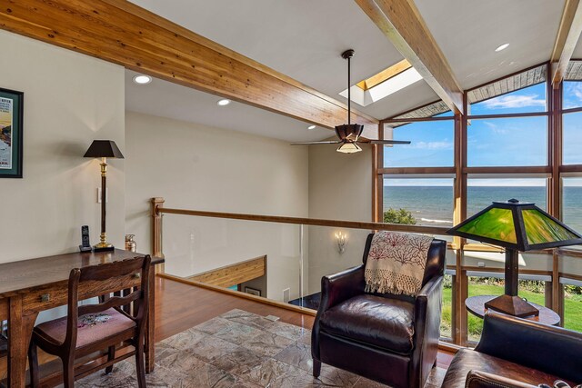 living area with wood-type flooring, a water view, ceiling fan, and lofted ceiling with skylight