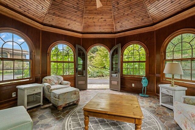 interior space featuring a towering ceiling, wood walls, and a healthy amount of sunlight