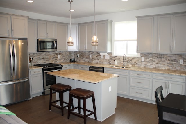 kitchen with a kitchen island, dark hardwood / wood-style flooring, pendant lighting, stainless steel appliances, and sink