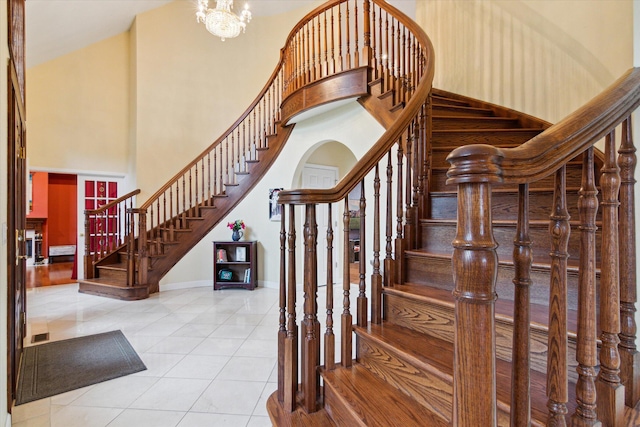 stairway with tile patterned flooring, a towering ceiling, and a notable chandelier