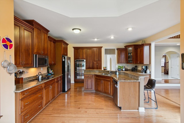 kitchen with a breakfast bar, kitchen peninsula, sink, light hardwood / wood-style flooring, and stainless steel appliances