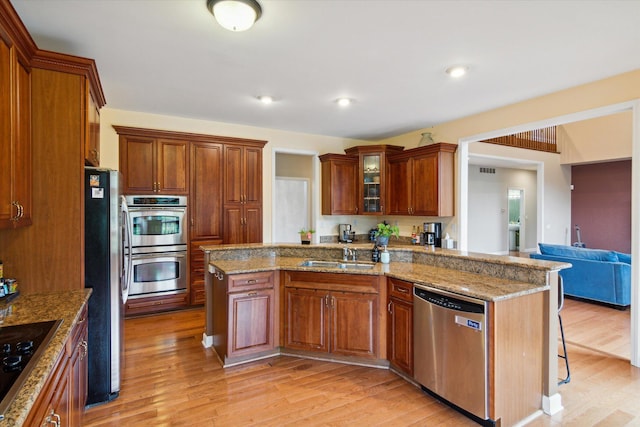 kitchen with a kitchen bar, kitchen peninsula, stainless steel appliances, light wood-type flooring, and sink