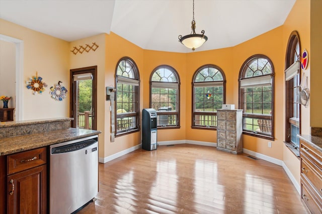 kitchen featuring stainless steel dishwasher, dark stone countertops, hanging light fixtures, and light hardwood / wood-style floors