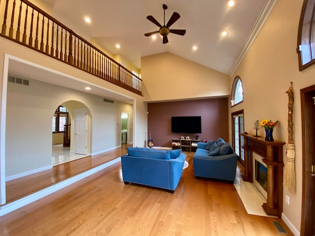 living room featuring ceiling fan, light hardwood / wood-style flooring, ornamental molding, and high vaulted ceiling