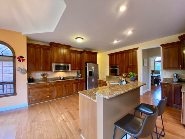 kitchen featuring a kitchen bar, light stone counters, stainless steel appliances, and light hardwood / wood-style floors