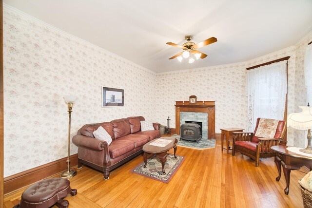 living room featuring a wood stove, crown molding, ceiling fan, and hardwood / wood-style floors