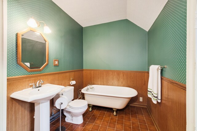 bathroom with wooden walls, a washtub, tile patterned floors, vaulted ceiling, and toilet