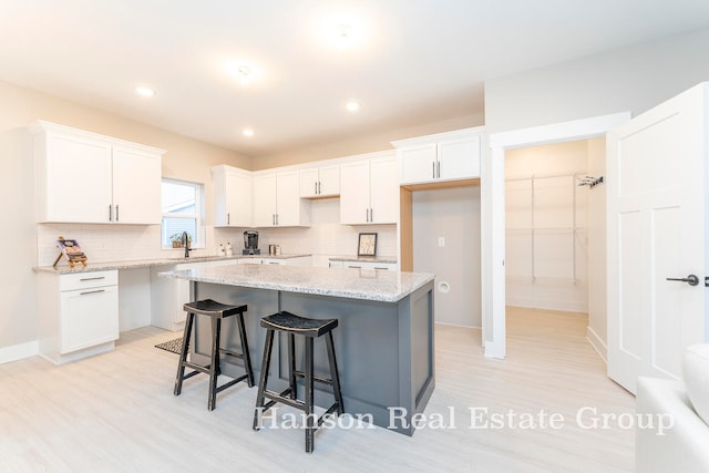 kitchen with light hardwood / wood-style flooring, a center island, decorative backsplash, and white cabinetry