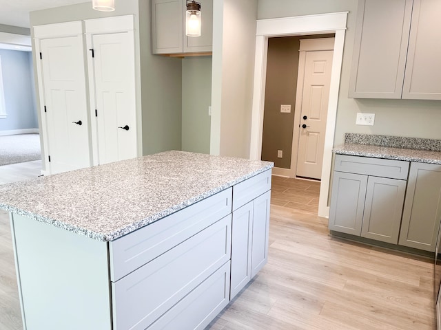 kitchen featuring light wood-type flooring, gray cabinetry, a kitchen island, and light stone counters