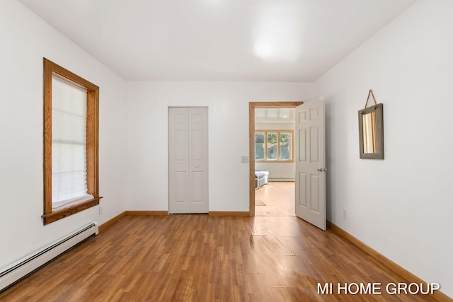 unfurnished bedroom with a closet, light hardwood / wood-style floors, and a baseboard heating unit