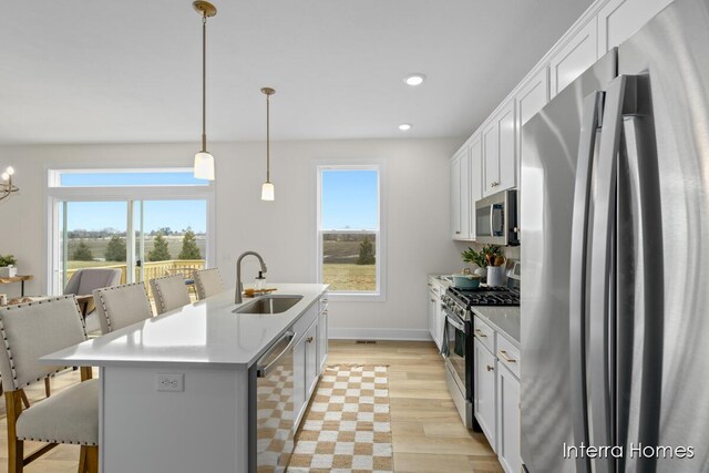 kitchen with appliances with stainless steel finishes, a kitchen breakfast bar, light wood-style floors, white cabinetry, and a sink