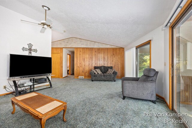 carpeted living room with a textured ceiling, visible vents, wooden walls, a ceiling fan, and lofted ceiling