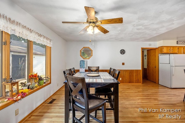 dining room with wooden walls, light wood-style floors, visible vents, ceiling fan, and wainscoting