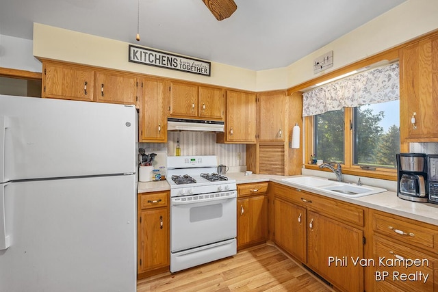 kitchen with light countertops, a sink, brown cabinets, under cabinet range hood, and white appliances