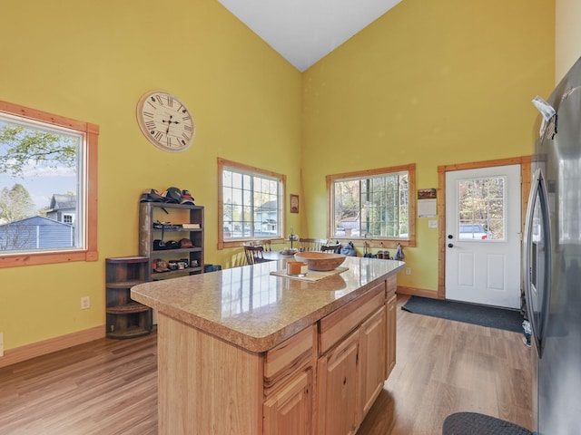 kitchen with a kitchen island, light hardwood / wood-style flooring, light brown cabinetry, high vaulted ceiling, and stainless steel refrigerator