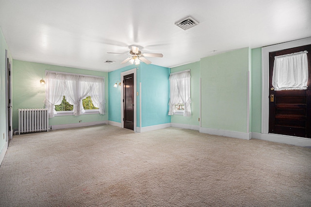 unfurnished room featuring ceiling fan, light colored carpet, and radiator heating unit