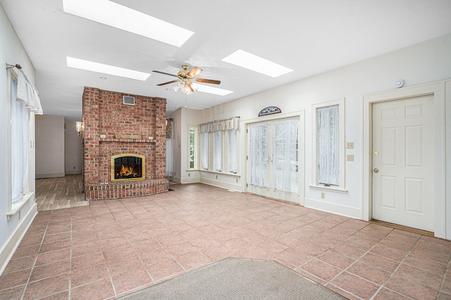 unfurnished living room featuring a fireplace, ceiling fan, and a skylight