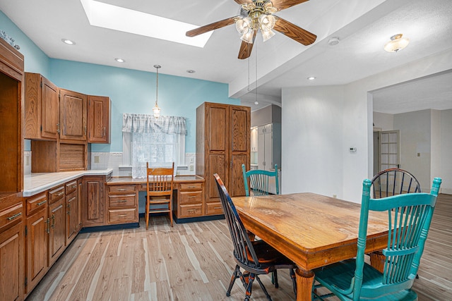 dining space with light wood-type flooring, built in desk, ceiling fan, and a skylight