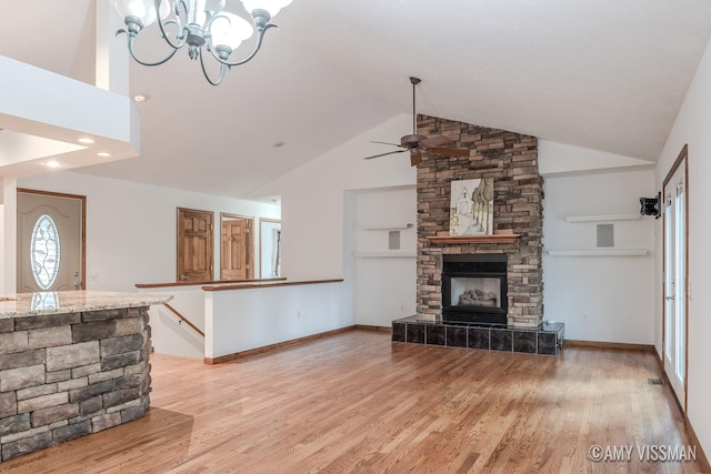 living room with ceiling fan with notable chandelier, a fireplace, high vaulted ceiling, and light hardwood / wood-style flooring